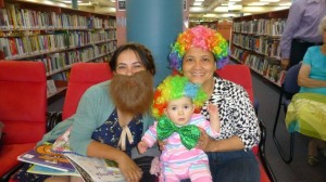 Rossal dressed as a bearded lady with Cecilia holding baby Trinity dressed as clowns for Storytime. 